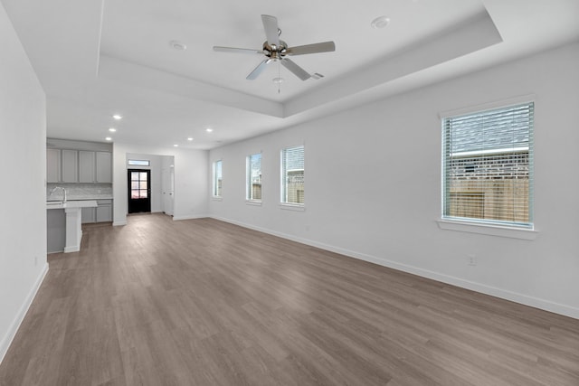 unfurnished living room with a tray ceiling, light wood-type flooring, and ceiling fan