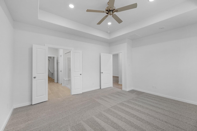 unfurnished bedroom with a tray ceiling, ceiling fan, and light carpet