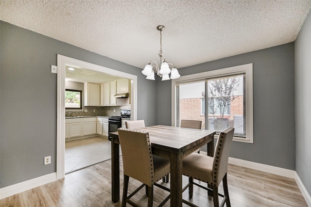 dining area with a textured ceiling, an inviting chandelier, and light hardwood / wood-style flooring