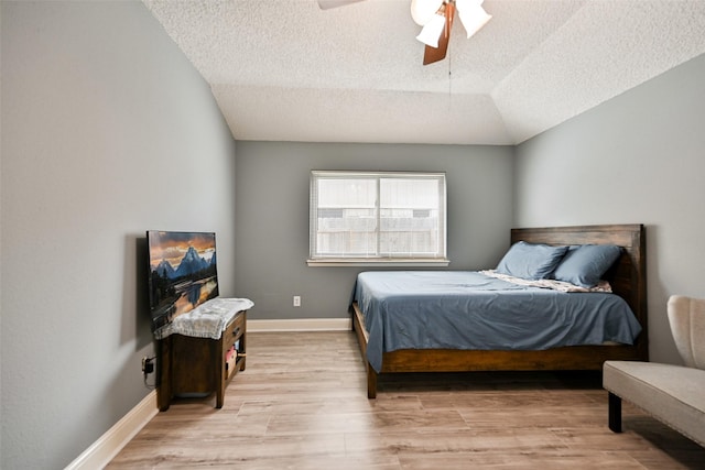 bedroom featuring ceiling fan, lofted ceiling, a textured ceiling, and light hardwood / wood-style floors