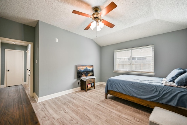 bedroom featuring ceiling fan, lofted ceiling, a textured ceiling, and light hardwood / wood-style flooring