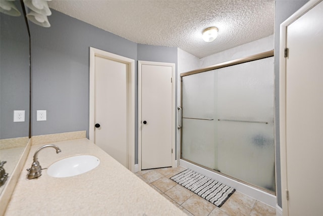 bathroom with tile patterned floors, a shower with door, a textured ceiling, and vanity