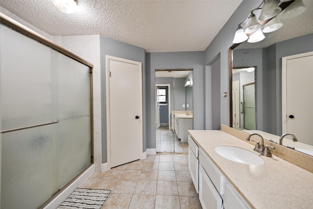 bathroom with tile patterned floors, vanity, a shower with door, and a textured ceiling