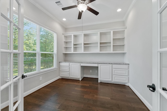 unfurnished office featuring built in desk, a healthy amount of sunlight, dark wood-type flooring, and ceiling fan