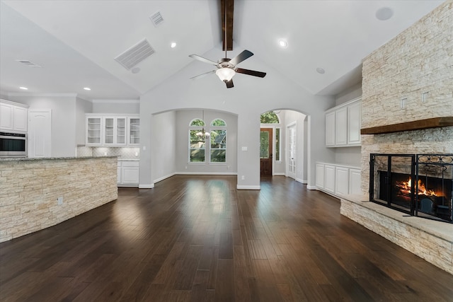 unfurnished living room with ceiling fan with notable chandelier, high vaulted ceiling, dark hardwood / wood-style floors, and a stone fireplace