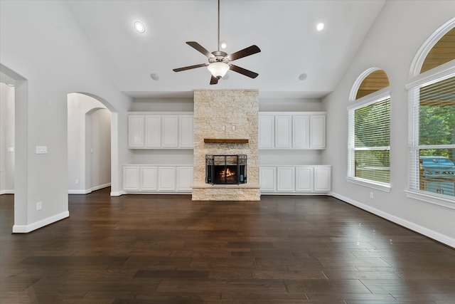 unfurnished living room featuring ceiling fan, a stone fireplace, dark hardwood / wood-style flooring, and high vaulted ceiling