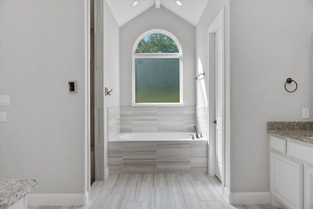 bathroom with tiled tub, vanity, and vaulted ceiling