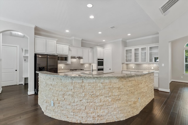 kitchen with light stone counters, dark wood-type flooring, white cabinetry, stainless steel appliances, and a spacious island