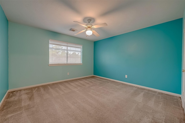 spare room with a ceiling fan, light colored carpet, visible vents, and baseboards