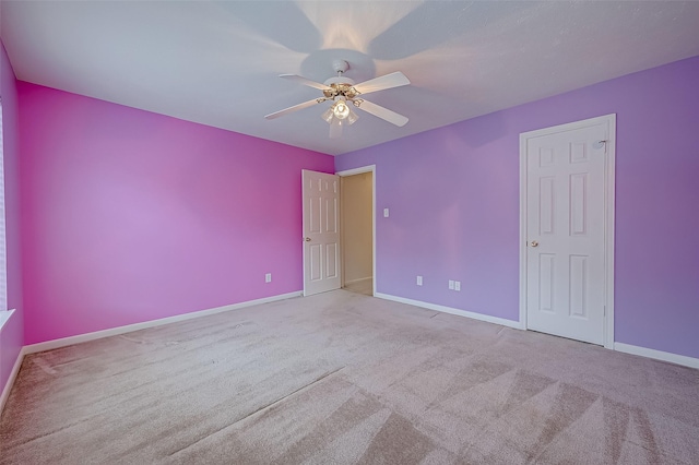 spare room featuring a ceiling fan, light colored carpet, and baseboards