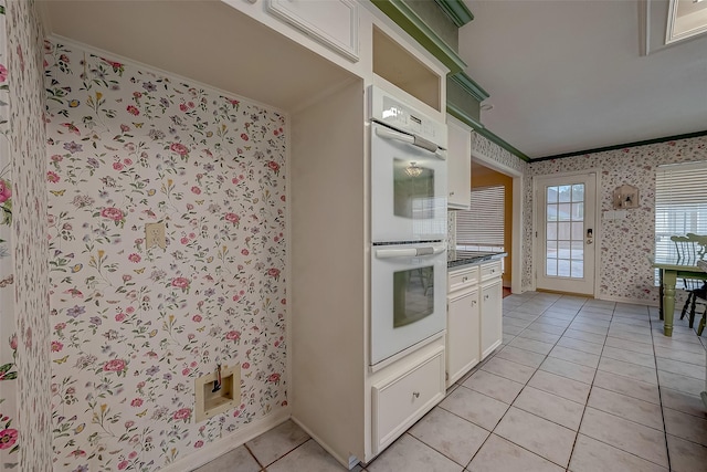 kitchen with wallpapered walls, light tile patterned floors, white double oven, dark countertops, and crown molding