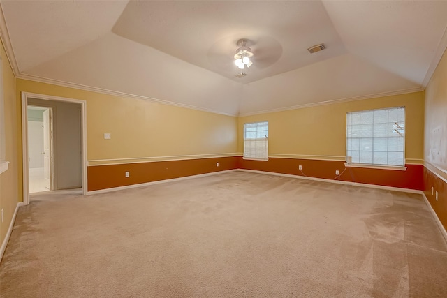 carpeted spare room featuring visible vents, a ceiling fan, vaulted ceiling, ornamental molding, and a tray ceiling