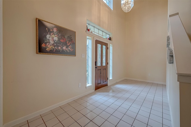 entryway with a towering ceiling, light tile patterned floors, baseboards, and an inviting chandelier