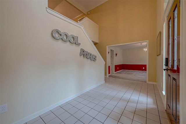 hallway with light tile patterned floors, a high ceiling, and baseboards