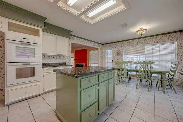 kitchen with double oven, a center island, white cabinetry, and wallpapered walls