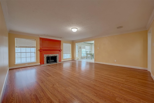 unfurnished living room with light wood-type flooring, a healthy amount of sunlight, crown molding, and baseboards