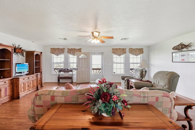 living room with light hardwood / wood-style flooring, a textured ceiling, and ceiling fan