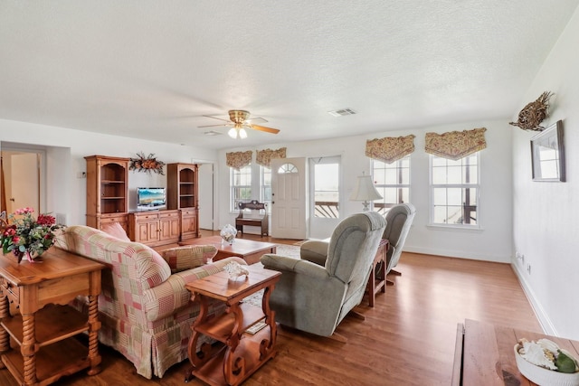 living room featuring baseboards, visible vents, ceiling fan, wood finished floors, and a textured ceiling