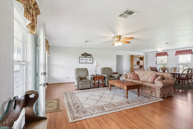 living room featuring light hardwood / wood-style flooring, a textured ceiling, and ceiling fan