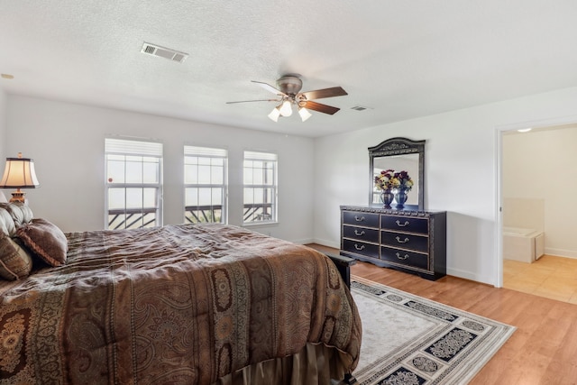 bedroom with a textured ceiling, light hardwood / wood-style flooring, ensuite bath, and ceiling fan