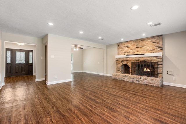 unfurnished living room with a brick fireplace, visible vents, baseboards, and wood finished floors