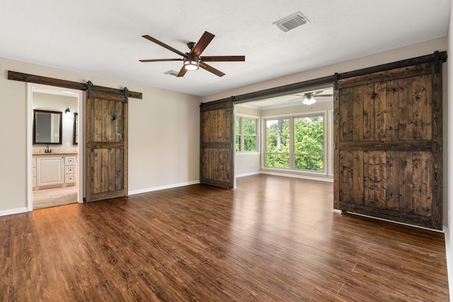 unfurnished living room featuring baseboards, a barn door, visible vents, and wood finished floors