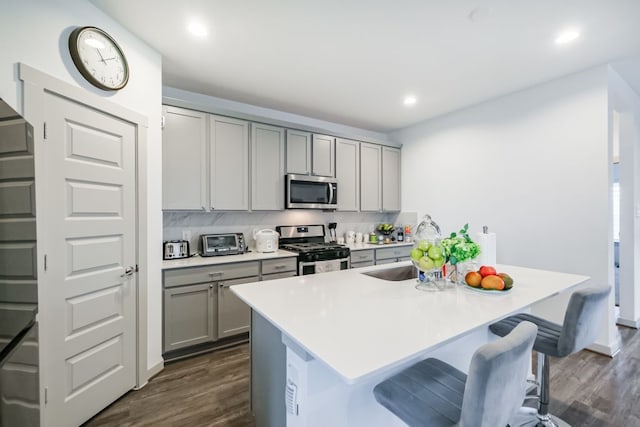 kitchen with a breakfast bar area, gray cabinets, dark hardwood / wood-style floors, stainless steel appliances, and decorative backsplash