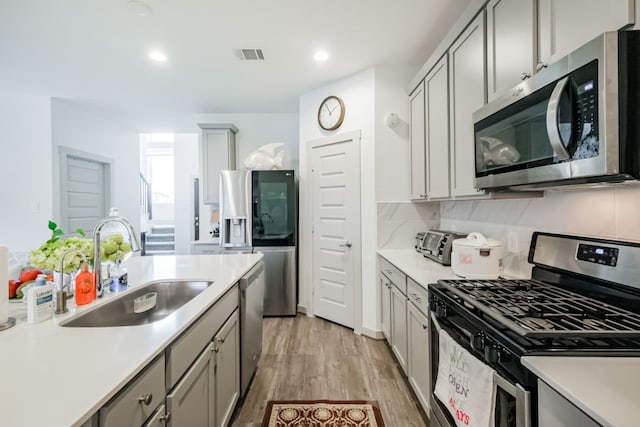 kitchen with gray cabinets, light wood-type flooring, sink, appliances with stainless steel finishes, and backsplash