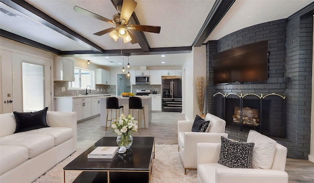 living room with beam ceiling, light hardwood / wood-style floors, sink, and a brick fireplace