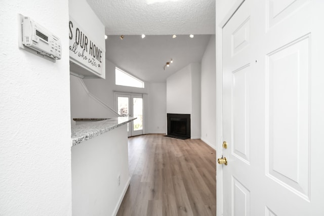 hallway featuring lofted ceiling, wood-type flooring, and a textured ceiling