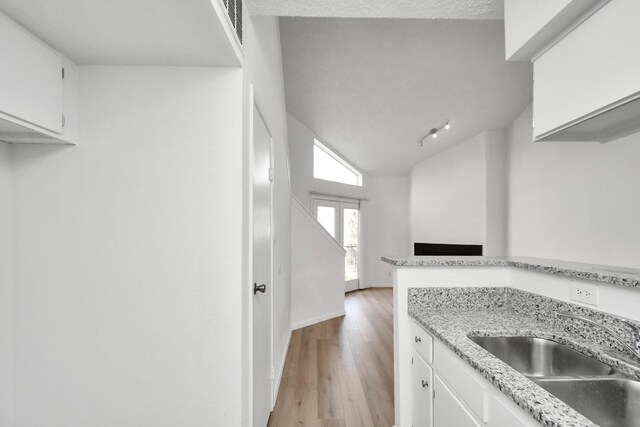 kitchen featuring white cabinets, rail lighting, sink, light hardwood / wood-style floors, and lofted ceiling