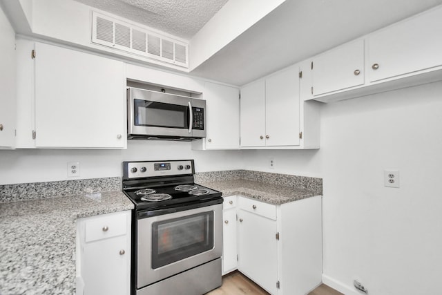 kitchen featuring white cabinetry, stainless steel appliances, light stone countertops, a textured ceiling, and light hardwood / wood-style flooring