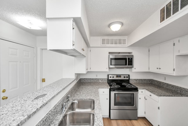 kitchen with stainless steel appliances, white cabinets, sink, light hardwood / wood-style floors, and a textured ceiling