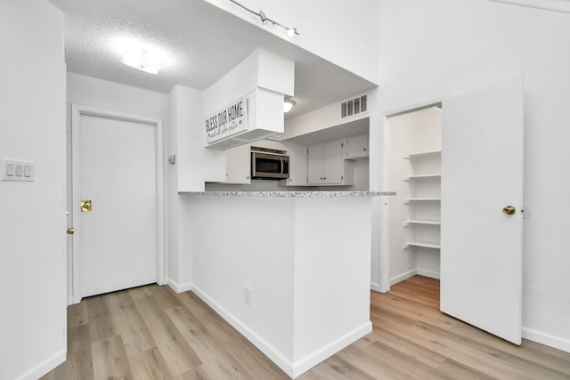 kitchen with rail lighting, kitchen peninsula, light wood-type flooring, and a textured ceiling