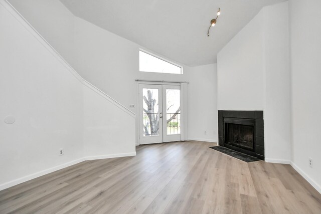 unfurnished living room featuring french doors, rail lighting, light wood-type flooring, a tiled fireplace, and lofted ceiling