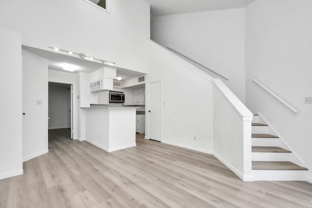 unfurnished living room with a high ceiling and light wood-type flooring