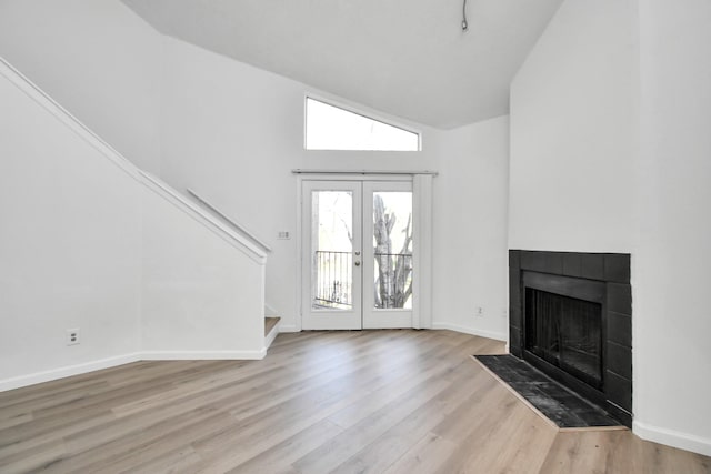 entryway featuring high vaulted ceiling, light hardwood / wood-style floors, a tile fireplace, and french doors