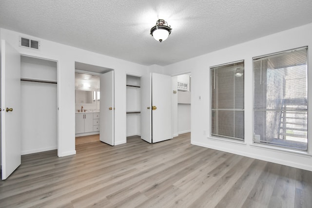 unfurnished bedroom with multiple closets, light hardwood / wood-style floors, ensuite bathroom, and a textured ceiling