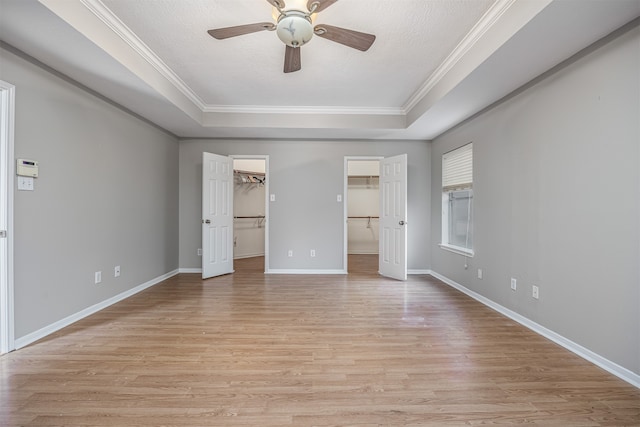 unfurnished bedroom featuring ceiling fan, a raised ceiling, light wood-type flooring, and a walk in closet