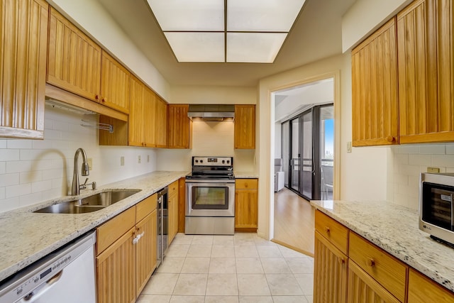 kitchen with wall chimney exhaust hood, light stone counters, stainless steel appliances, and a sink