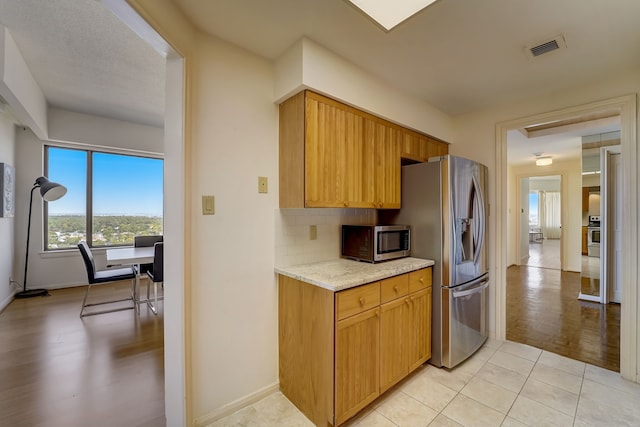 kitchen featuring light stone counters, light tile patterned floors, stainless steel appliances, visible vents, and backsplash