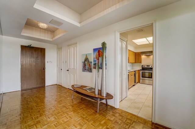 hall with a raised ceiling, visible vents, and baseboards