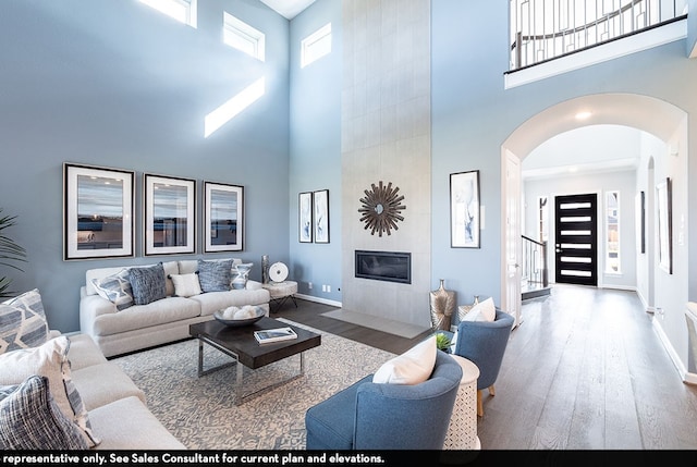 living room with wood-type flooring, a tile fireplace, and a high ceiling