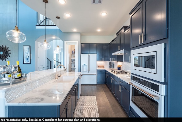 kitchen with appliances with stainless steel finishes, sink, hanging light fixtures, dark hardwood / wood-style floors, and light stone countertops