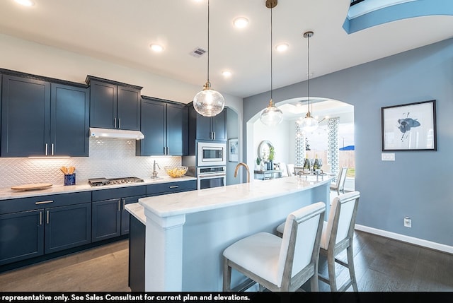 kitchen with decorative light fixtures, tasteful backsplash, stainless steel appliances, a kitchen bar, and a center island with sink