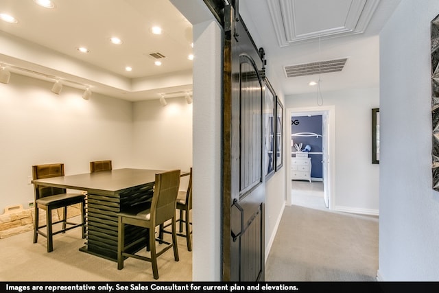 dining space with track lighting, a barn door, and light colored carpet