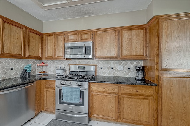 kitchen with light tile patterned flooring, dark stone counters, decorative backsplash, and appliances with stainless steel finishes