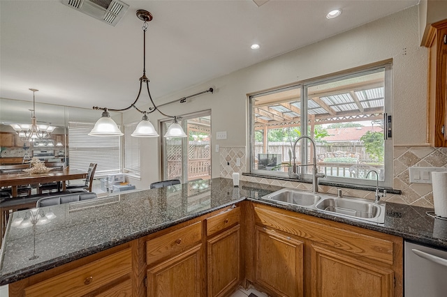 kitchen featuring dark stone countertops, tasteful backsplash, kitchen peninsula, hanging light fixtures, and sink