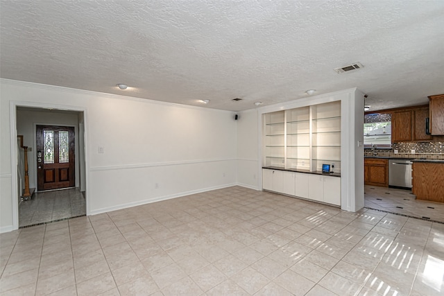 unfurnished living room with a textured ceiling, sink, light tile patterned floors, and ornamental molding