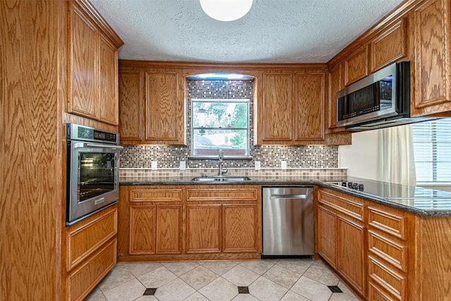 kitchen with dark stone counters, light tile patterned floors, appliances with stainless steel finishes, and sink